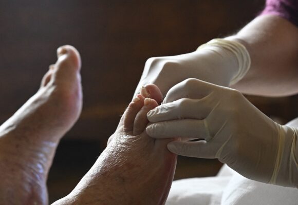Une aide-soignante soigne le pied d’une personne âgée lors d’une visite à domicile, reflet du besoin croissant de soutien médical à domicile pour les personnes agées. Paris. 17 octobre 2025. Photo : Eric Beracassat / Hans Lucas via AFP